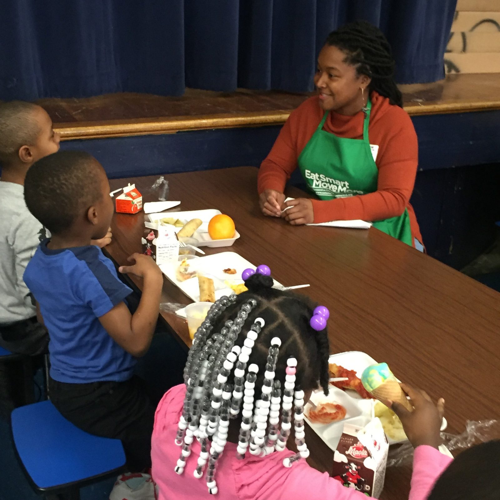 An adult woman talks to three children while they eat