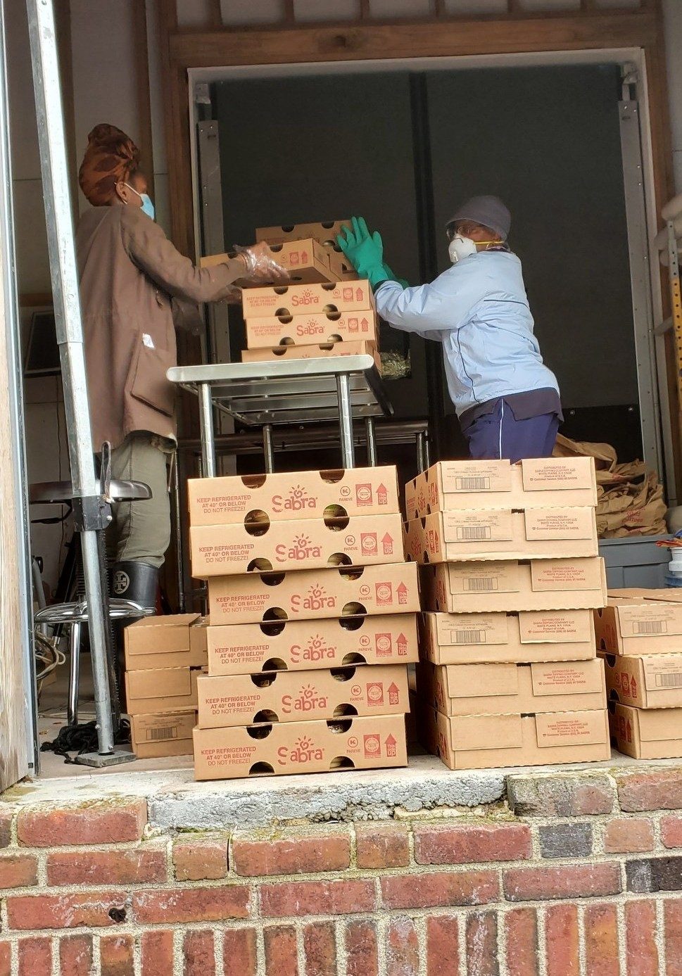 Two women unload boxes of Sabra hummus donated to the Urban Ag Center