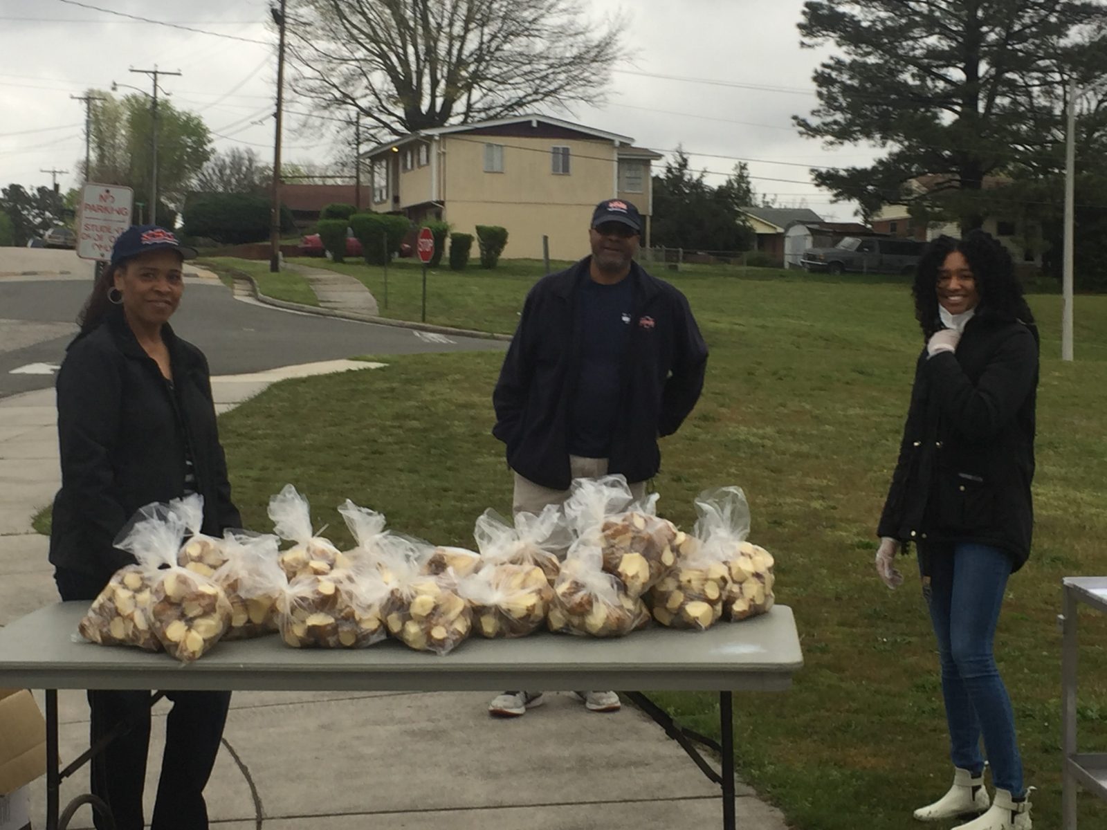 Three food volunteers display the bags of potatoes ready to be picked up by those in need