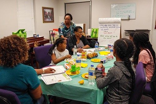 Adults and children sitting at a table learning about healthy food