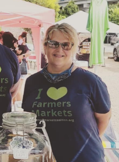 A woman in sunglasses smiling at a farmers market